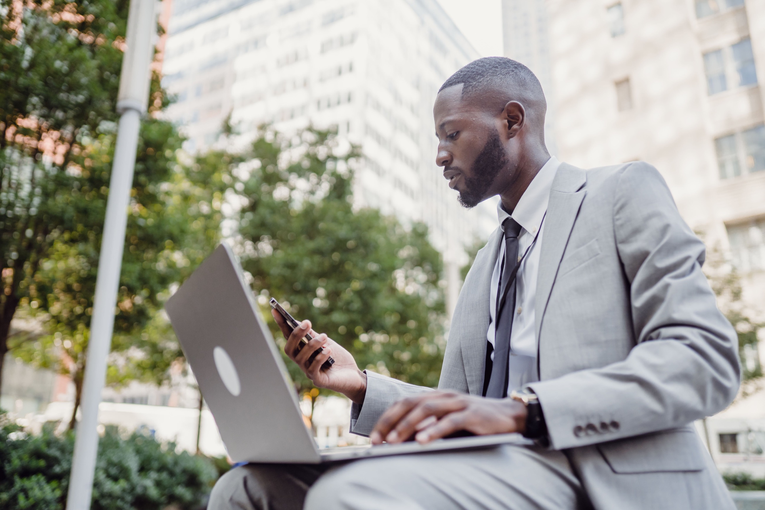 A Black business professional working outside with a laptop and phone.